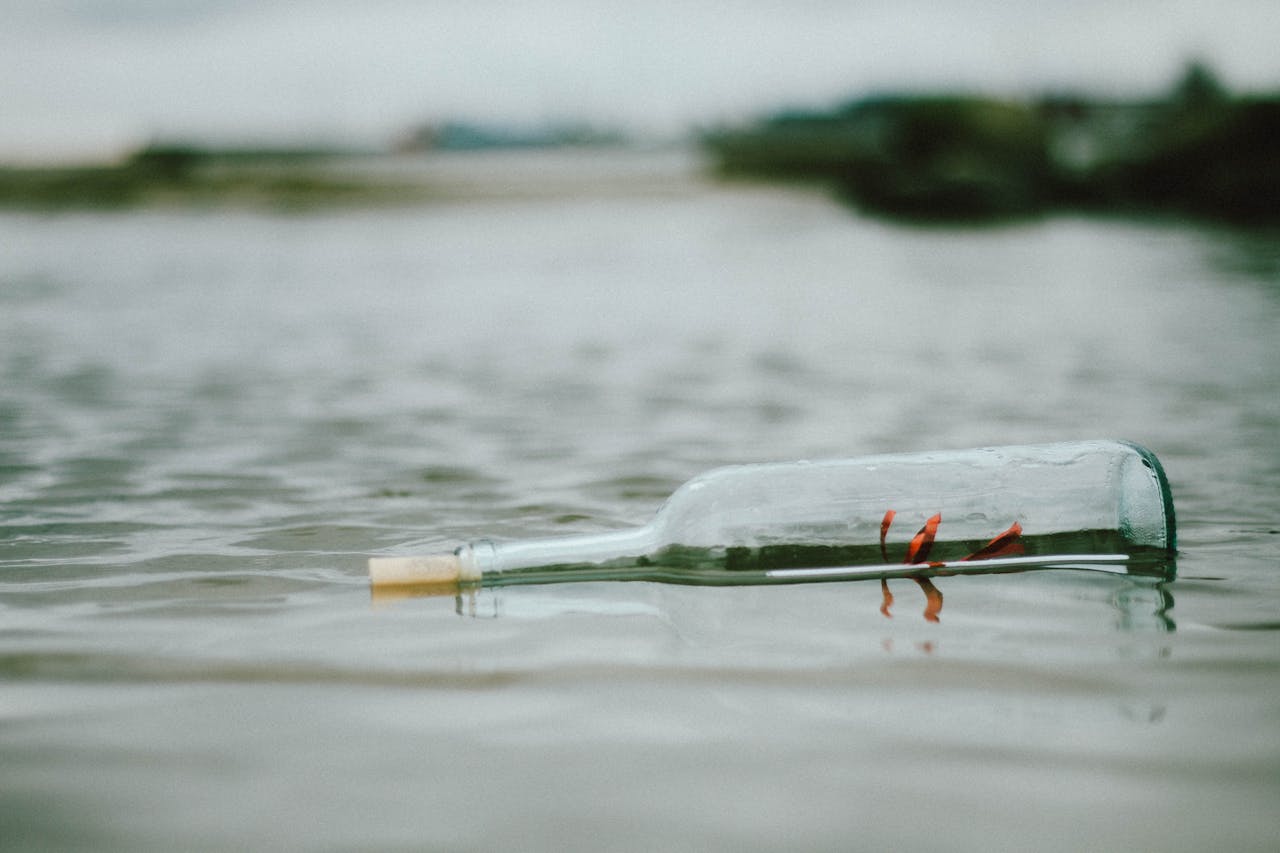 A glass bottle with a letter inside floats on a tranquil water surface, creating a sense of mystery.